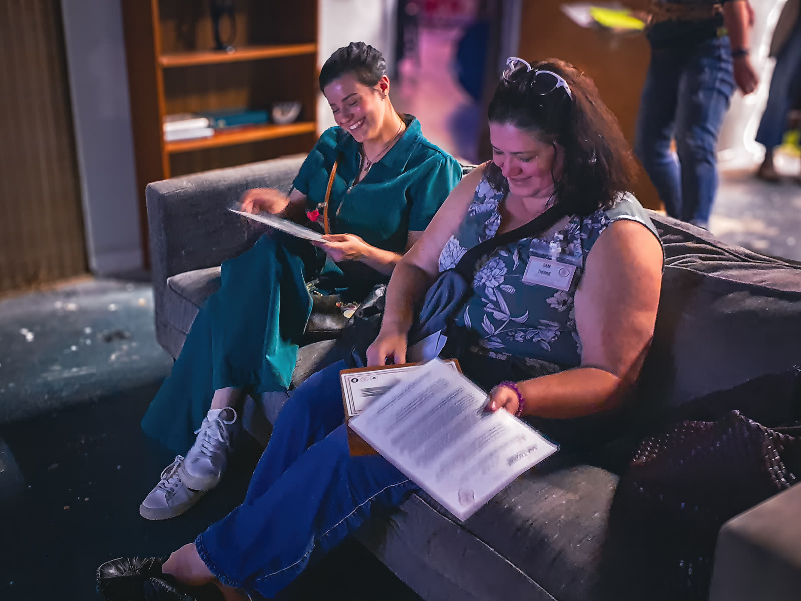 Two players laughing comfortably on a couch while reading character briefs