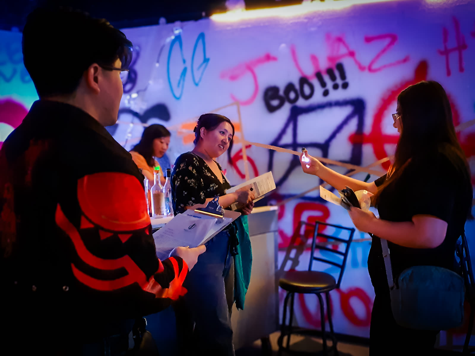 A player reaching across with a clipboard, accusing another player at the graffiti-walled venue